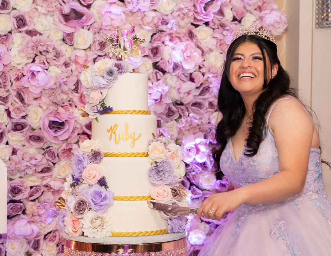 Celebrant with tiered cake against a rose wall